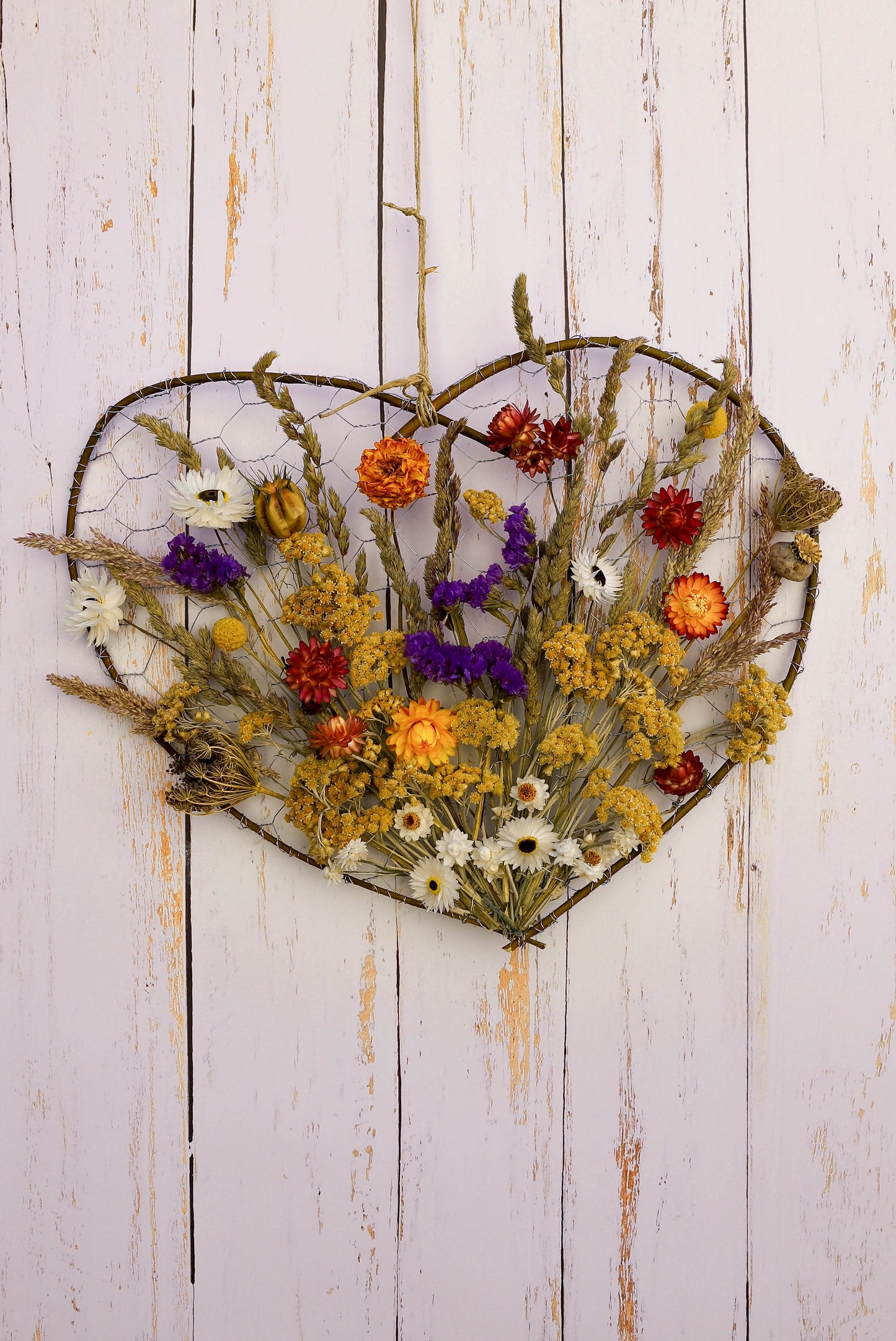 couronne en forme de coeur réalisée avec des sarments de saule et du grillage sur laquelle sont fixées de fleurs séchées colorées