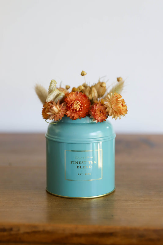 fleurs séchées dans les tons orangés présentées dans une boite à thé en métal bleu / vert