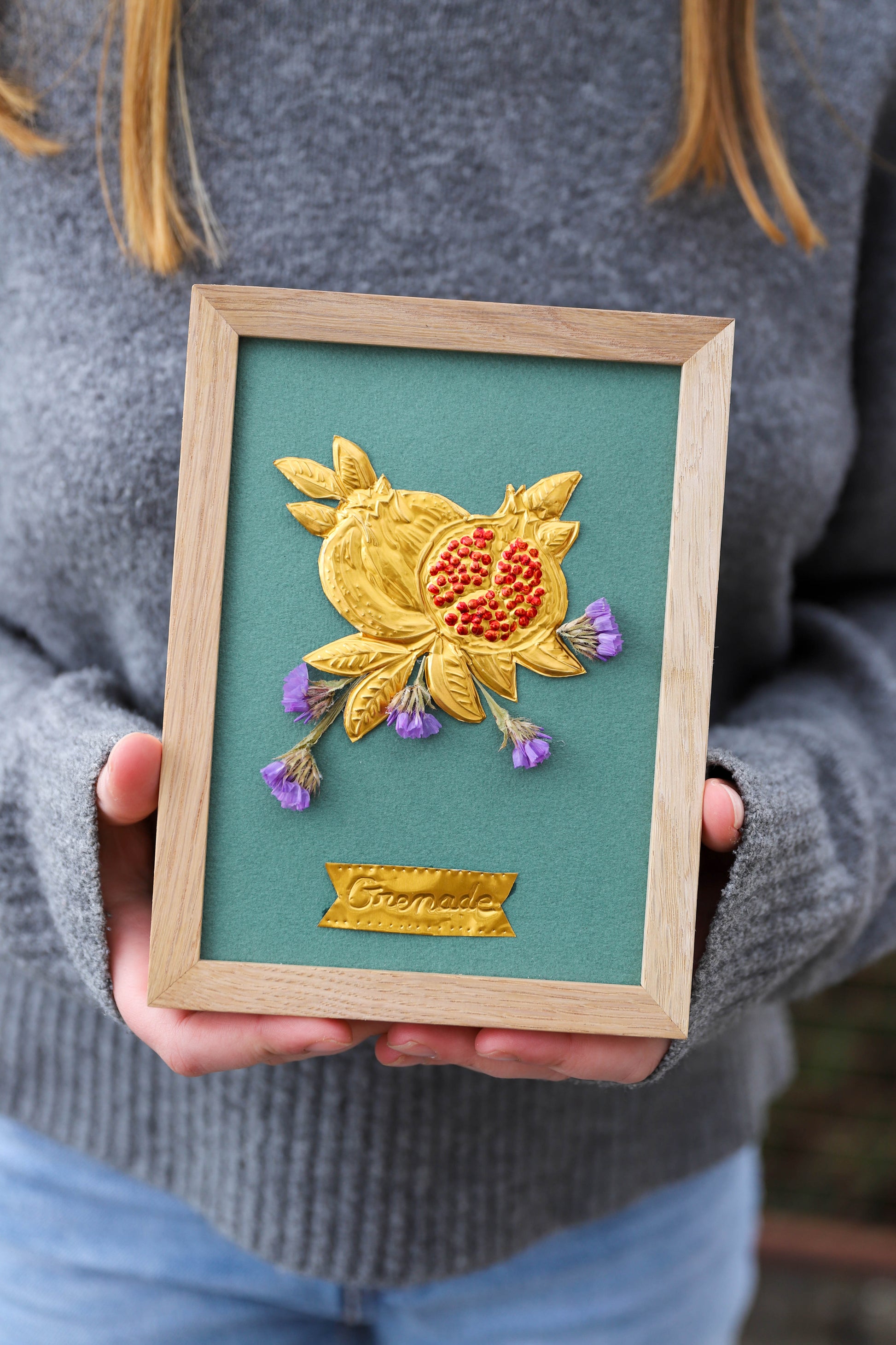cadre en chêne clair avec un motif de fruit réalisé sur du métal repoussé. Les graines de la grenade sont peintes avec une couleur adaptée en couleur rouge. Le motif est agrémenté de fleurs séchées violettes