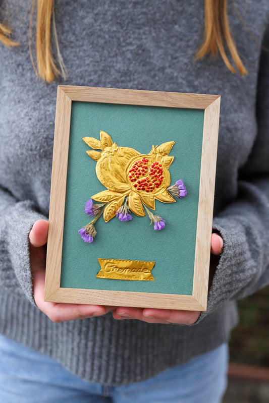 cadre en chêne clair avec un motif de fruit réalisé sur du métal repoussé. Les graines de la grenade sont peintes avec une couleur adaptée en couleur rouge. Le motif est agrémenté de fleurs séchées violettes