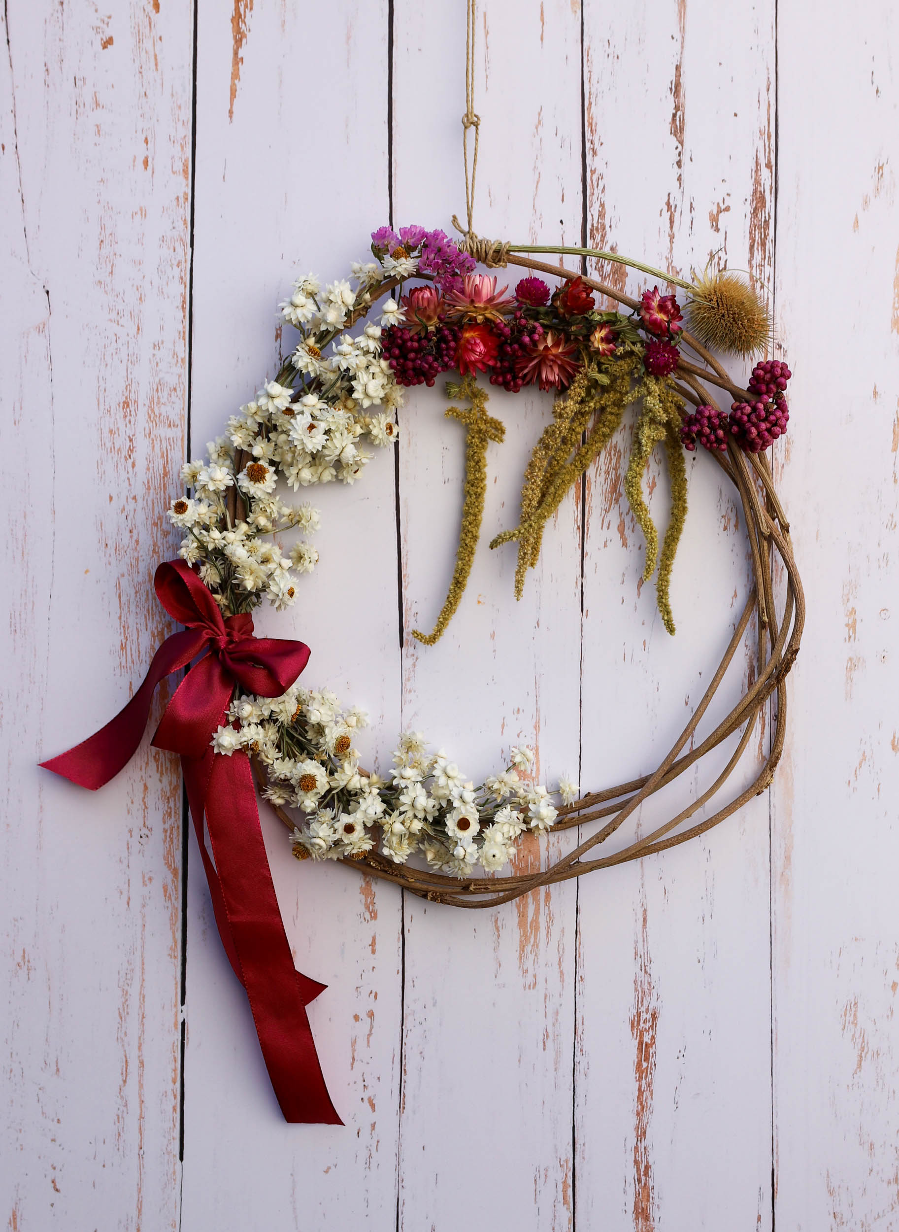 couronne de fleurs séchées avec des fleurs blanches, roses, des chardons, des baies violettes et des fleurs qui pendent