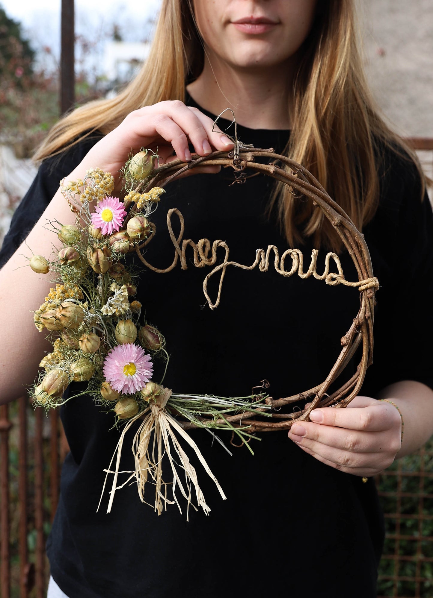 couronne réalisée avec des fleurs séchées . Il y a écrit "chez nous" avec des lettres en ficelle armée