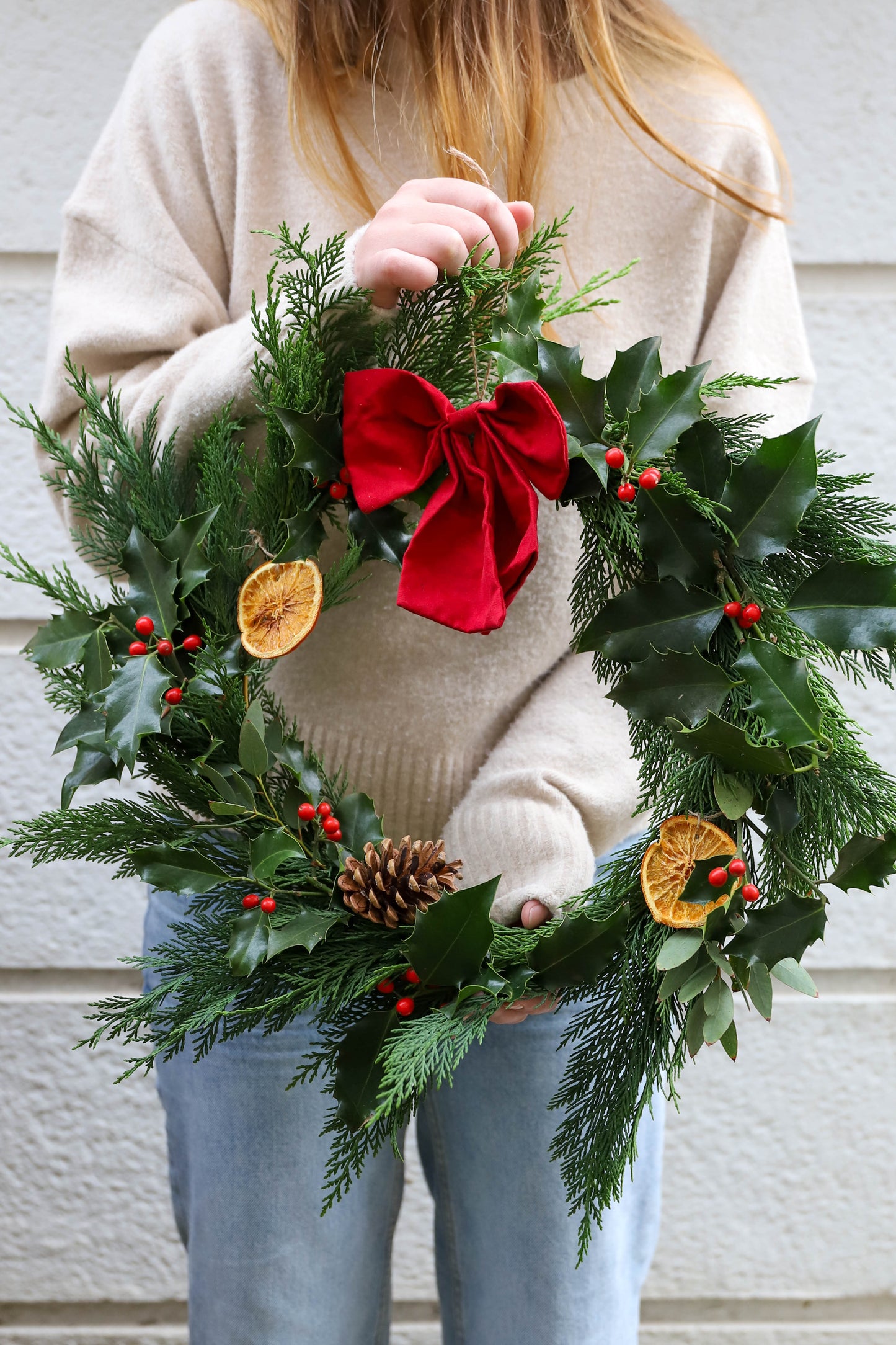 couronne de Noël française avec des branches de sapin, du houx, des branches d'eucalyptus, des tranches d'oranges séchées et un gros noeud rouge