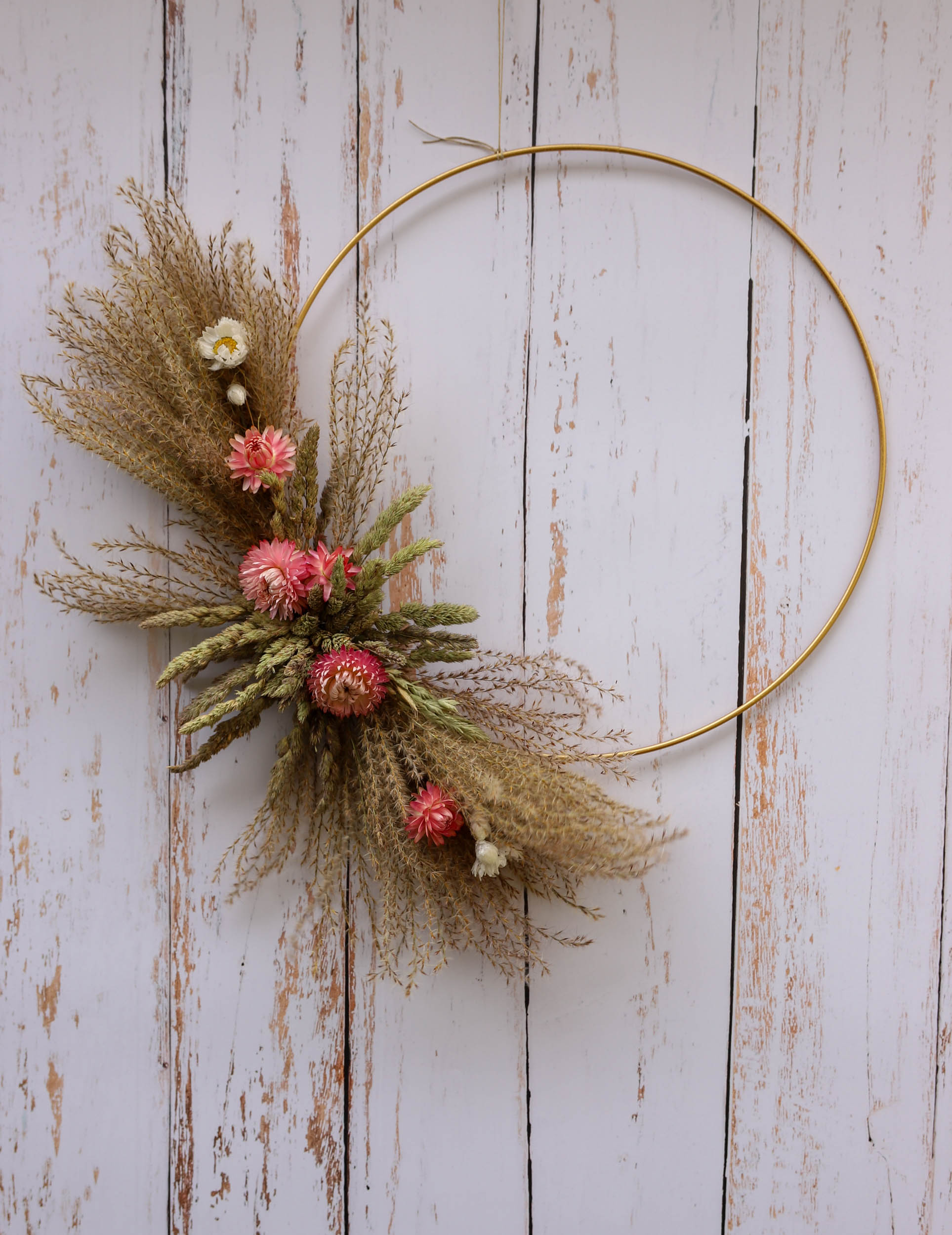 couronne avec des plumeaux et des fleurs séchées roses sur un cercle en métal