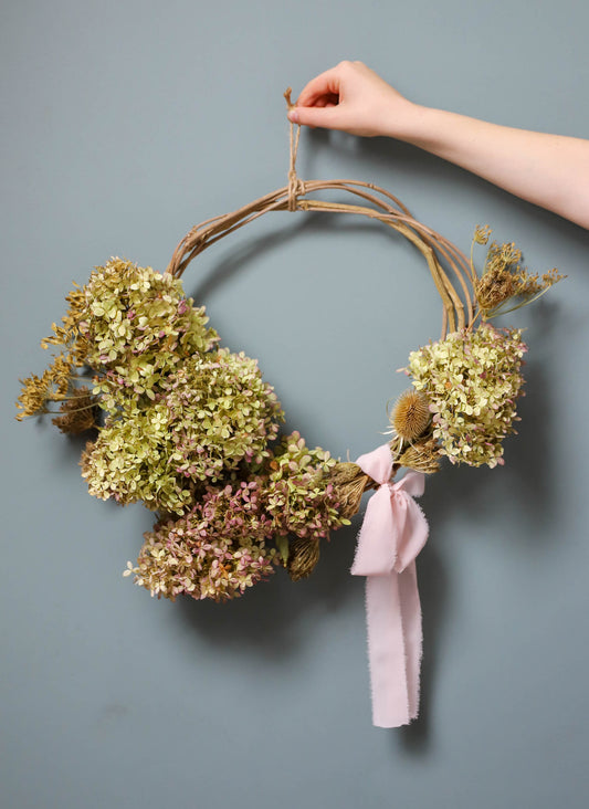 couronne de fleurs d'hortensias avec un gros ruban rose sur une base réalisée avec des sarments