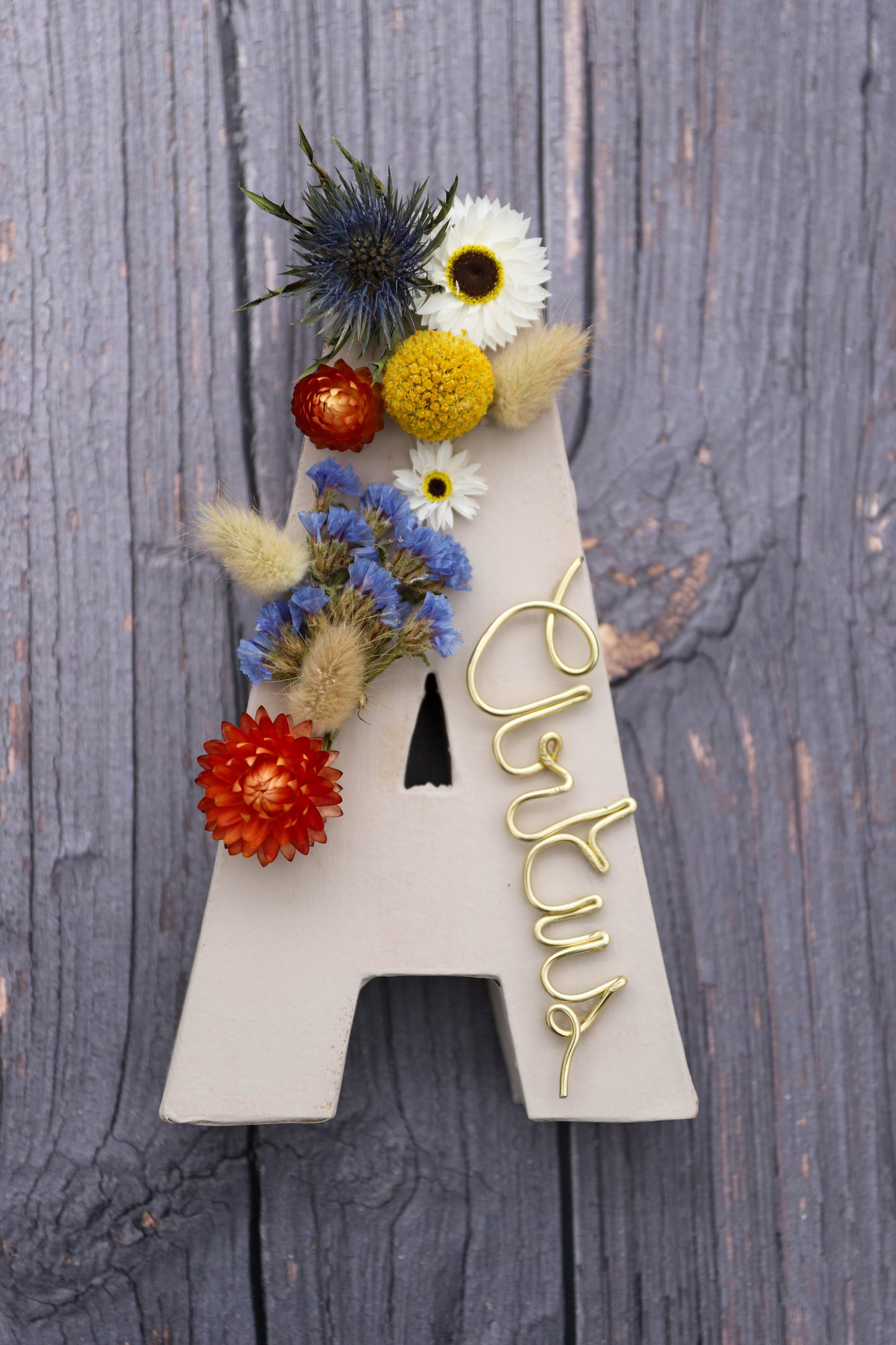 grande lettre en carton décorée avec des fleurs séchées colorées bleues jaunes et oranges et le prénom écrit avec du fils d'aluminium doré